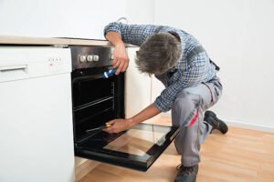 full length of repairman examining oven with flashlight in kitchen